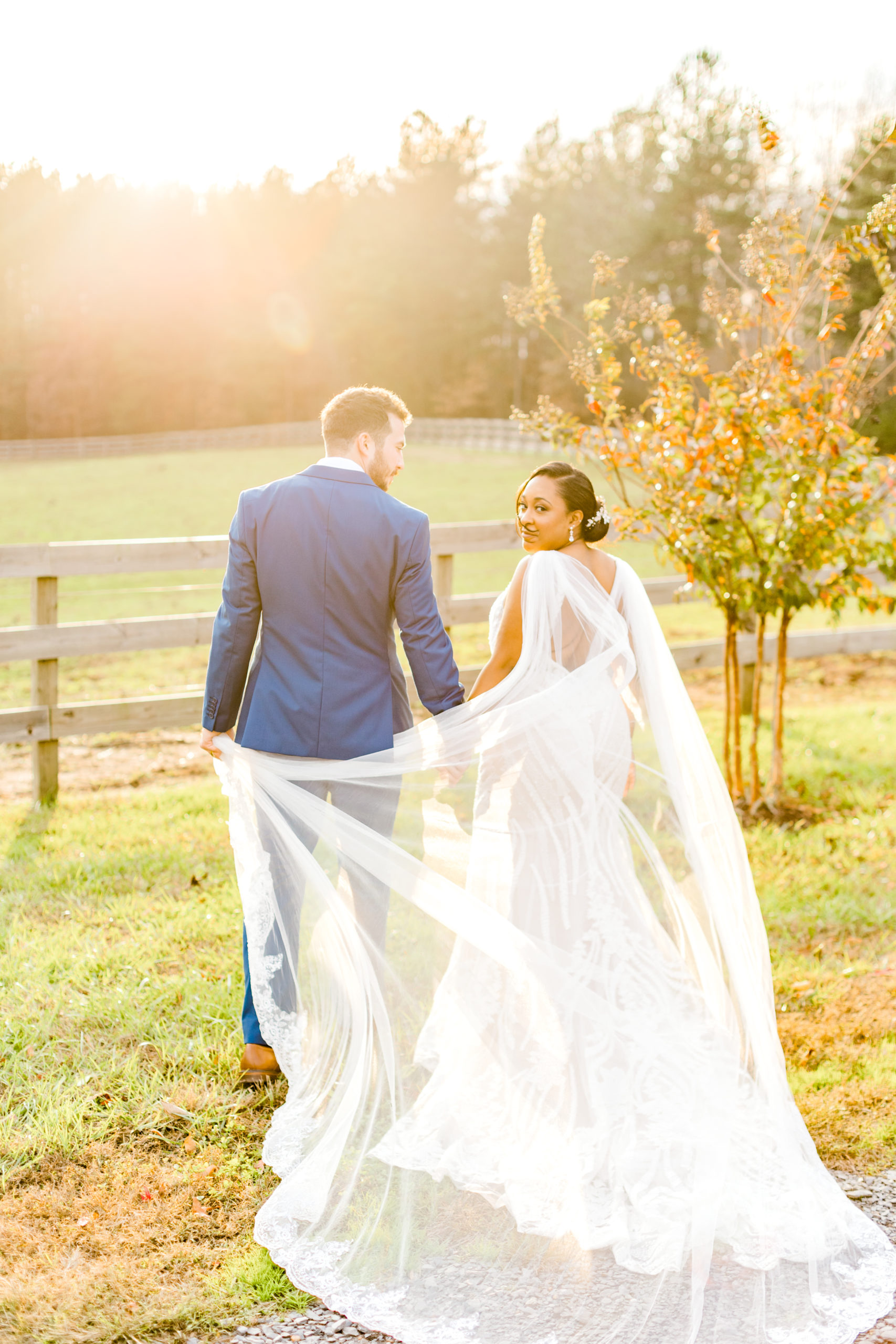 Interracial wedding couple walking into sunset, bride turned and smiling towards the camera